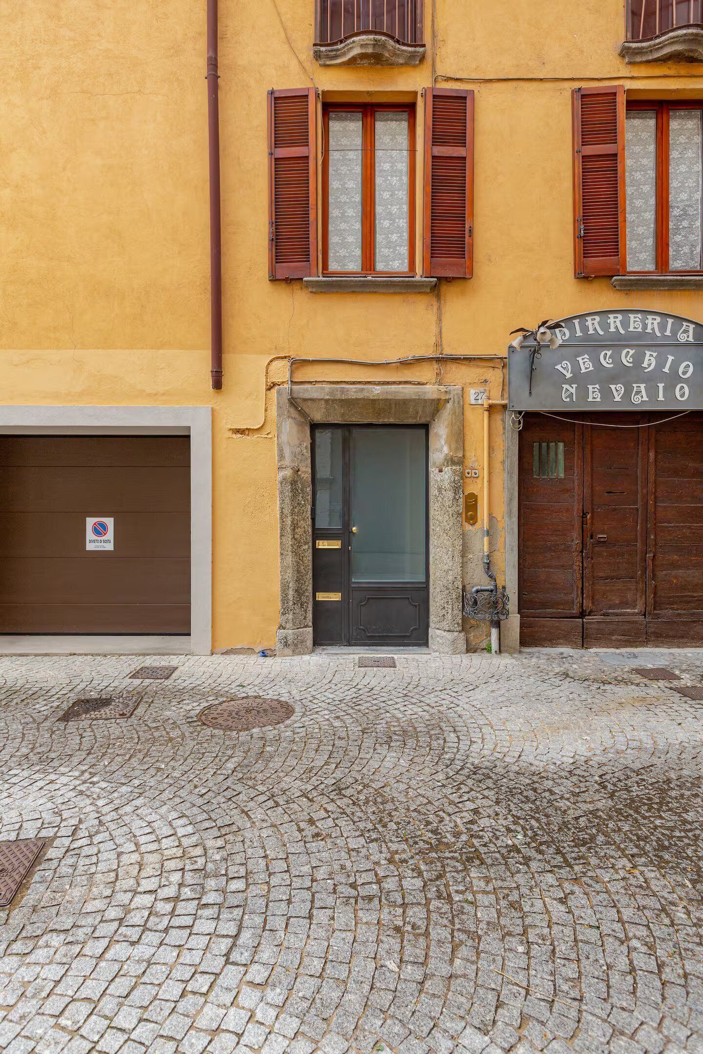 Ein Gebäude mit geschlossenem Garagentor, einer schwarzen Tür und einer gepflasterten Straße.