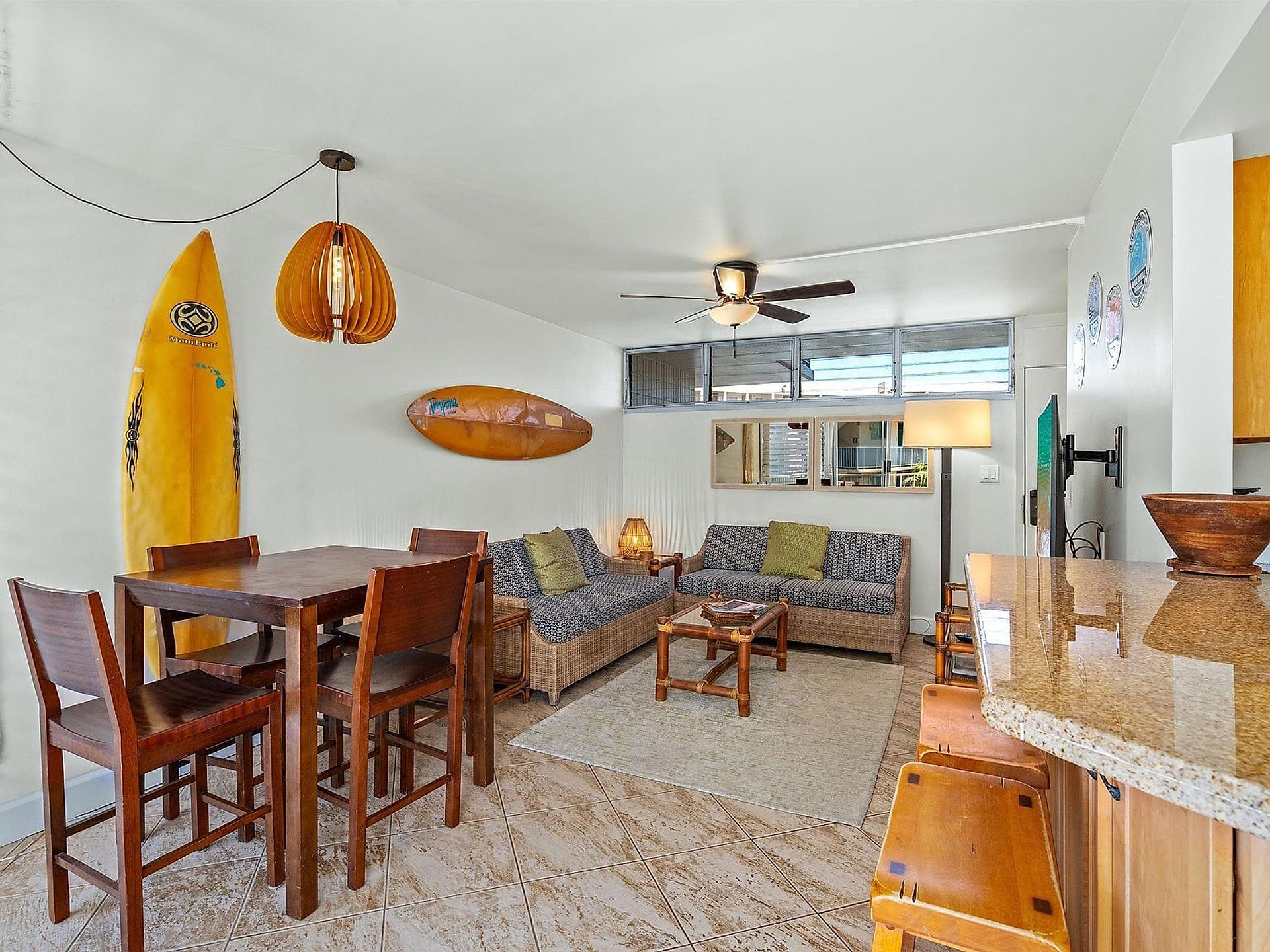 Uma sala de estar ampla com uma mesa de jantar, cadeiras, sofá e ventilador de teto.