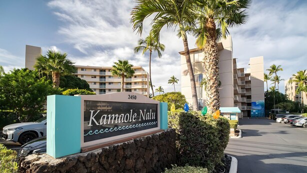 A sign for 'Kamaole Nalu' with a stone wall and palm trees in the foreground. - Beachfront 4BR, 2 Condos for 12 in Kihei! (Kihei)