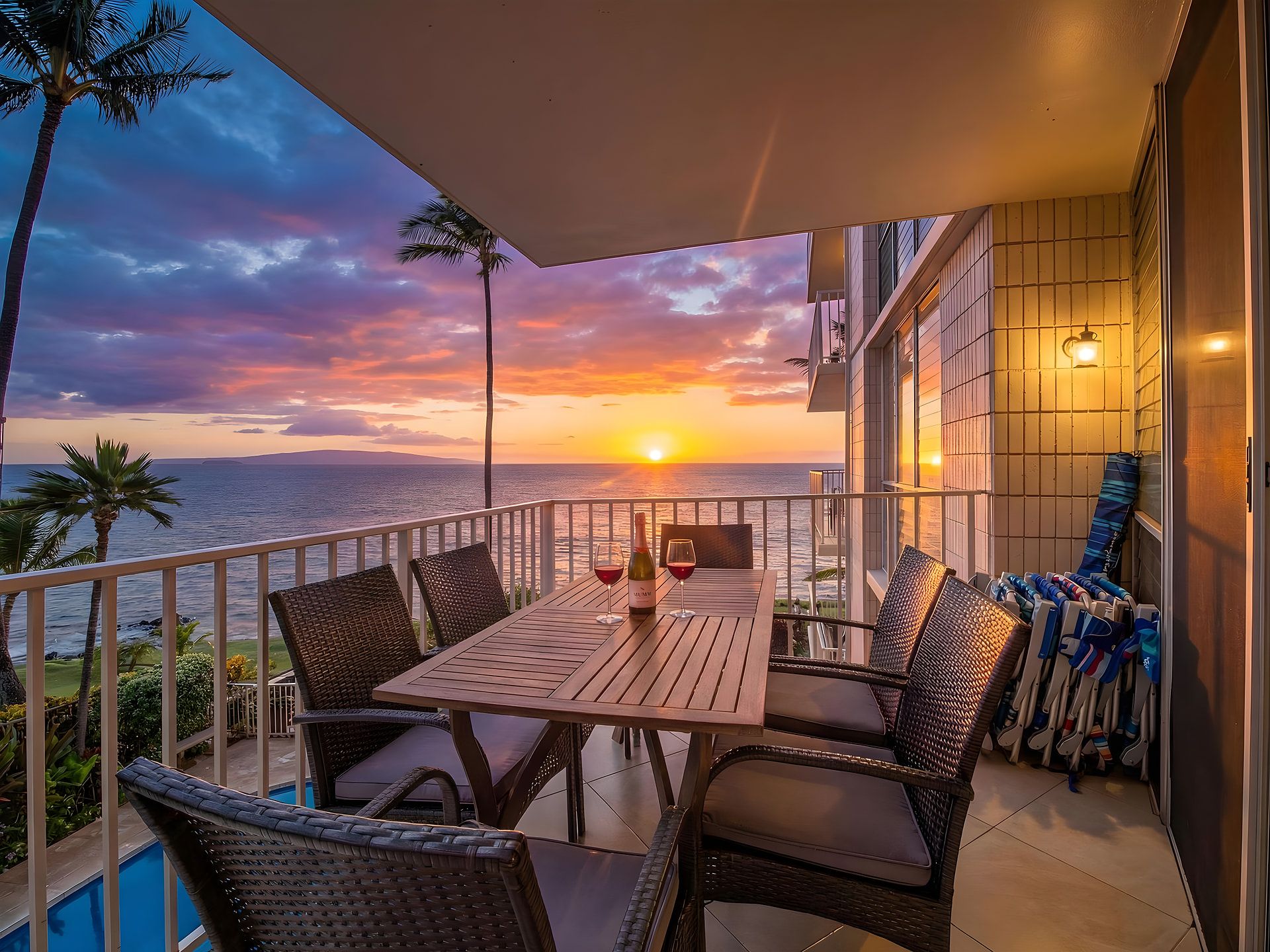 A balcony with a table and chairs, a bottle of wine, and a view of the sunset over the ocean.