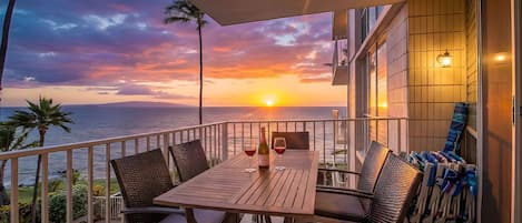 Un balcon avec une table et des chaises, une bouteille de vin et une vue sur le coucher de soleil sur l’océan.