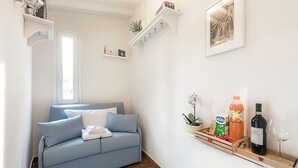 Uma sala de estar moderna com um sofá azul, uma mesinha lateral, uma prateleira na parede com diversos objetos e um quadro emoldurado.