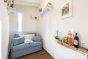 Ein modernes Wohnzimmer mit einem blauen Sofa, einem kleinen Beistelltisch, einer Wandregal mit verschiedenen Gegenständen und einem gerahmten Bild.