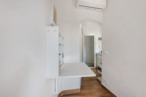 Un pasillo estrecho con un estante blanco, una puerta al final y un equipo de aire acondicionado blanco montado en la pared.
