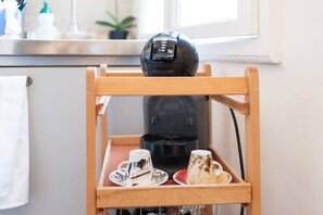 Ein Holzregal mit einer Kaffeemaschine und zwei Tassen, eine mit Untertasse, die andere ohne.