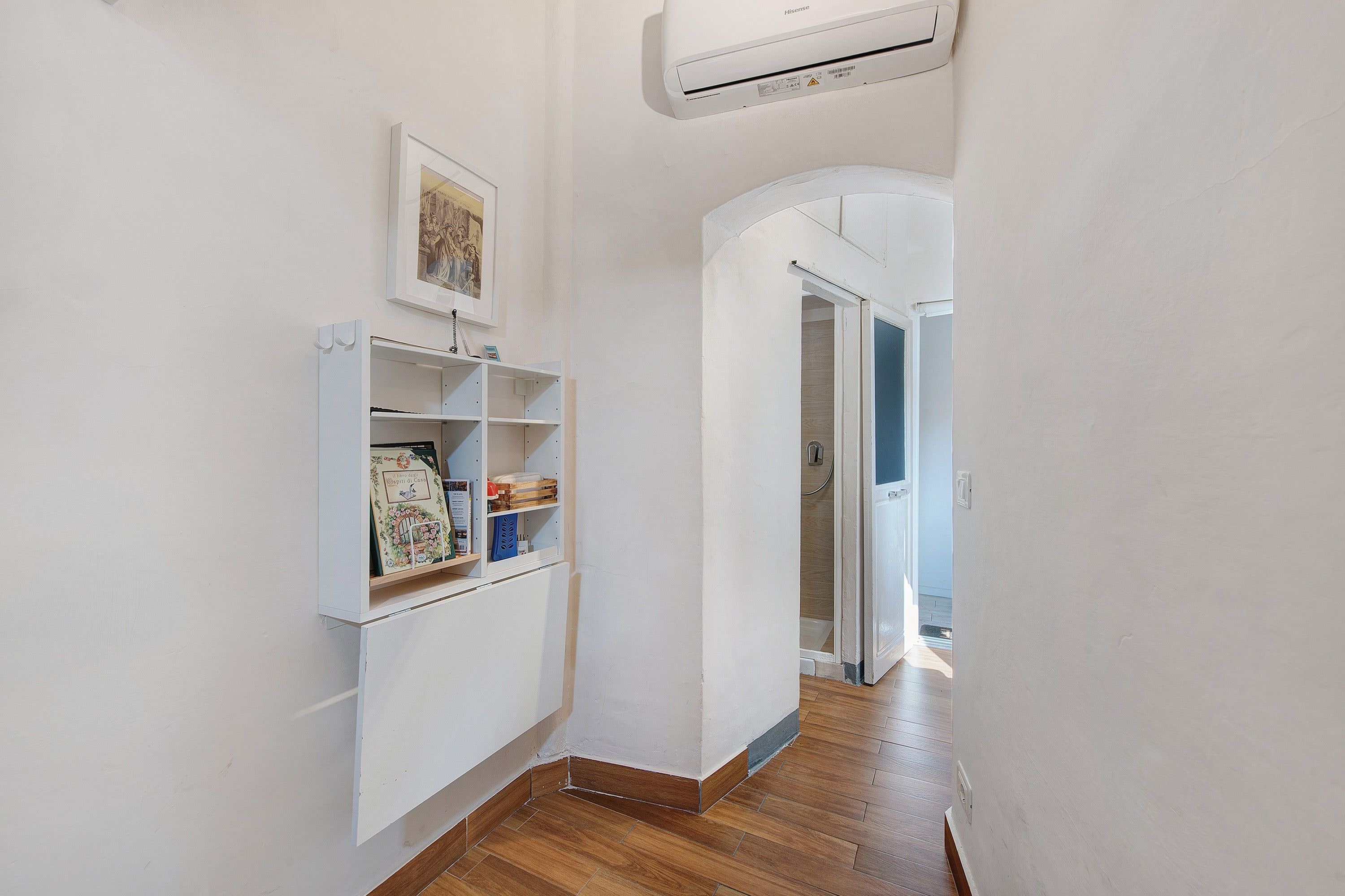 A narrow hallway with a white wall, a mounted air conditioner, and a door leading to another room.