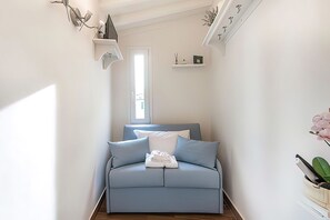 Ein kleines, hellblaues Schlafsofa mit Kissen und einem gefalteten Handtuch, eine weiße Tür und ein kleines Regal mit einem Bilderrahmen und einer Pflanze.