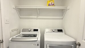 A laundry room with two white front-loading washing machines and a shelf above them. - Luxe Family Retreat -Sleeps 10 - Large Home - Game Room -Private Back Yard (McKinney)