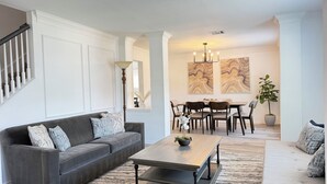 A living room with a gray sofa, a wooden coffee table, and a dining area with a table and chairs. - Luxe Family Retreat -Sleeps 10 - Large Home - Game Room -Private Back Yard (McKinney)