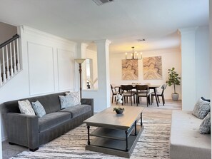 Ein Wohnzimmer mit grauem Sofa, einem Holztisch und einem Essbereich mit Tisch und Stühlen.