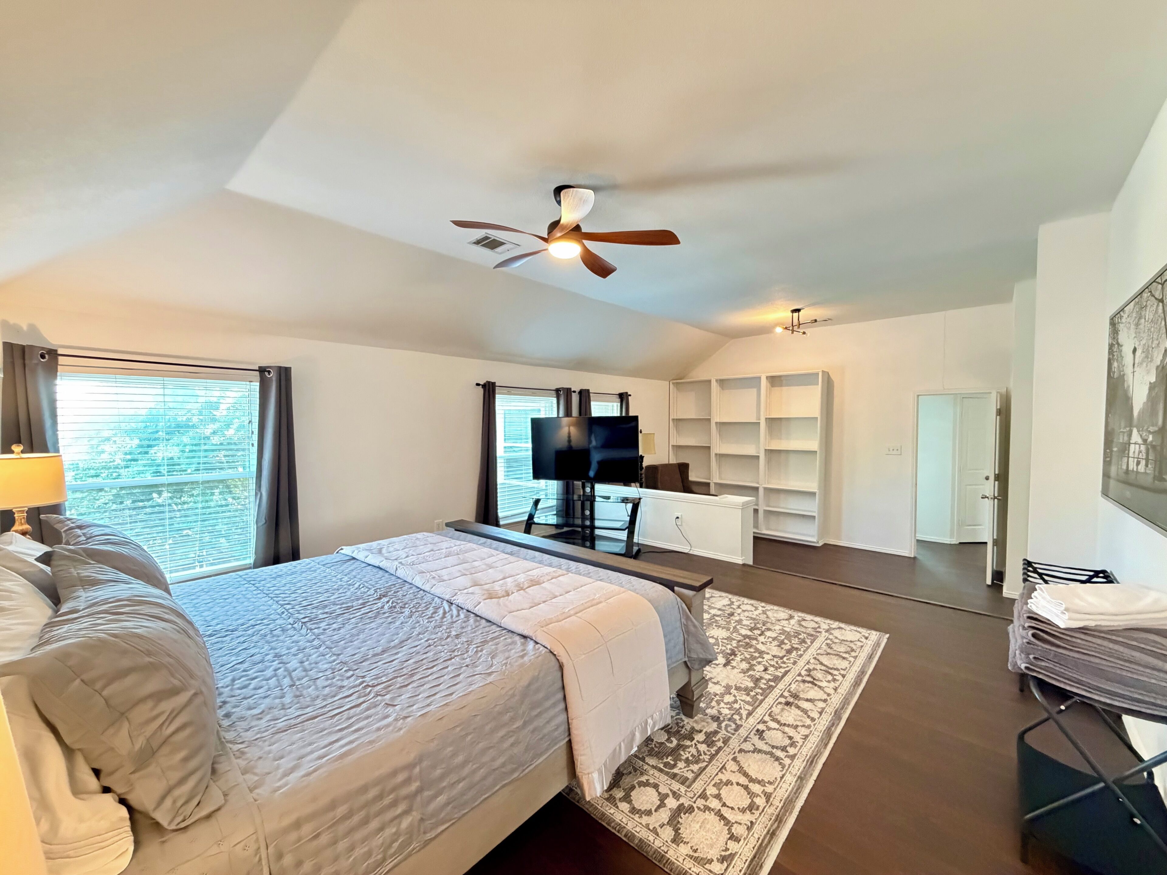 A bedroom with a bed, a desk, a chair, a television, and a ceiling fan.