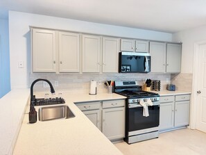 A modern kitchen with white cabinetry, stainless steel appliances, and a black faucet. - Luxe Family Retreat -Sleeps 10 - Large Home - Game Room -Private Back Yard (McKinney)