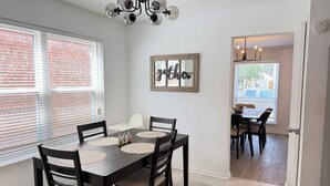 A dining area with a dark wooden table and chairs, a chandelier, and a view of the outside through a window. - Luxe Family Retreat -Sleeps 10 - Large Home - Game Room -Private Back Yard (McKinney)