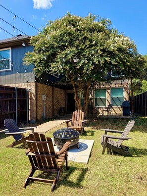 A backyard with outdoor seating, a fire pit, and a tree providing shade. - Luxe Family Retreat -Sleeps 10 - Large Home - Game Room -Private Back Yard (McKinney)