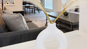 A living room with a white vase on a table, a grey sofa, and a dining area in the background. - Luxe Family Retreat -Sleeps 10 - Large Home - Game Room -Private Back Yard (McKinney)