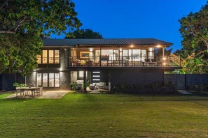 A modern two-story house with a balcony, a well-maintained lawn, and a large window overlooking the yard. - Oceanfront 5-Bedroom Home with Direct Beach Access in Paia (Paia)