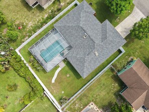 Luchtbeeld van een woonhuis met zwembad, overdekt terras en omheinde tuin.