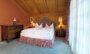 A bedroom with a wooden ceiling, a bed with a patterned bed skirt, two bedside tables with lamps, and a dresser. - AN EXCEPTIONAL COMBINATION OF SPACE, COMFORT & ALPINE ELEGANCE ,MATTERHORN VIEWS (Zermatt)