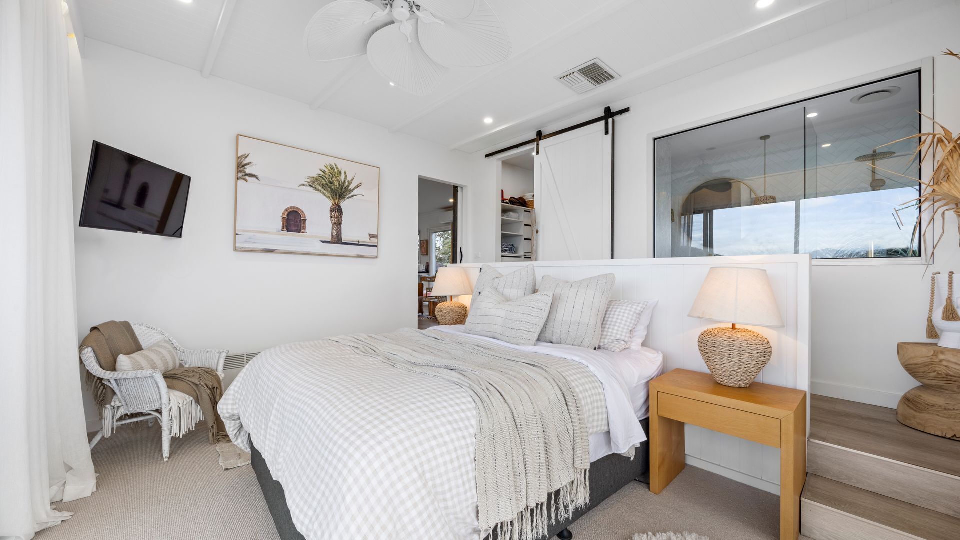 A modern bedroom with a bed, bedside tables, a chair, a TV, and artwork on the wall.