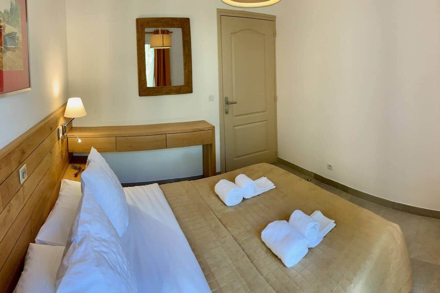 A hotel room with a bed, a bedside table, a mirror, and a door.