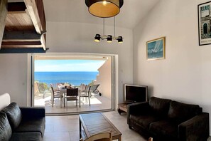 Un salon avec vue sur la mer, un coin repas avec des sièges à l’extérieur, une télévision et un canapé.