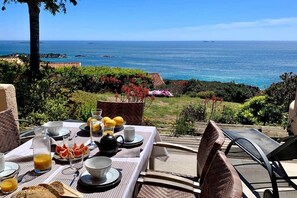 Ein Essbereich im Freien mit einem für das Frühstück gedeckten Tisch, mit Blick auf die Küste.