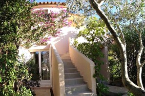 A staircase leading to a building with a white exterior and a balcony with pink flowers. - Casa di Toro:House in front of the sea at Palombaggia, 2/8 p (Porto-Vecchio)