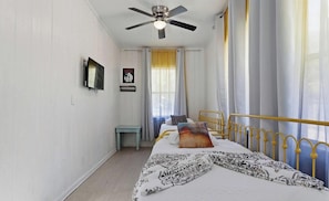A bedroom with a bed, a ceiling fan, a small table, and a window with curtains.