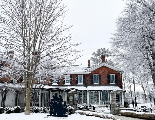 A brick building with a gabled roof and large windows, surrounded by snow-covered trees.