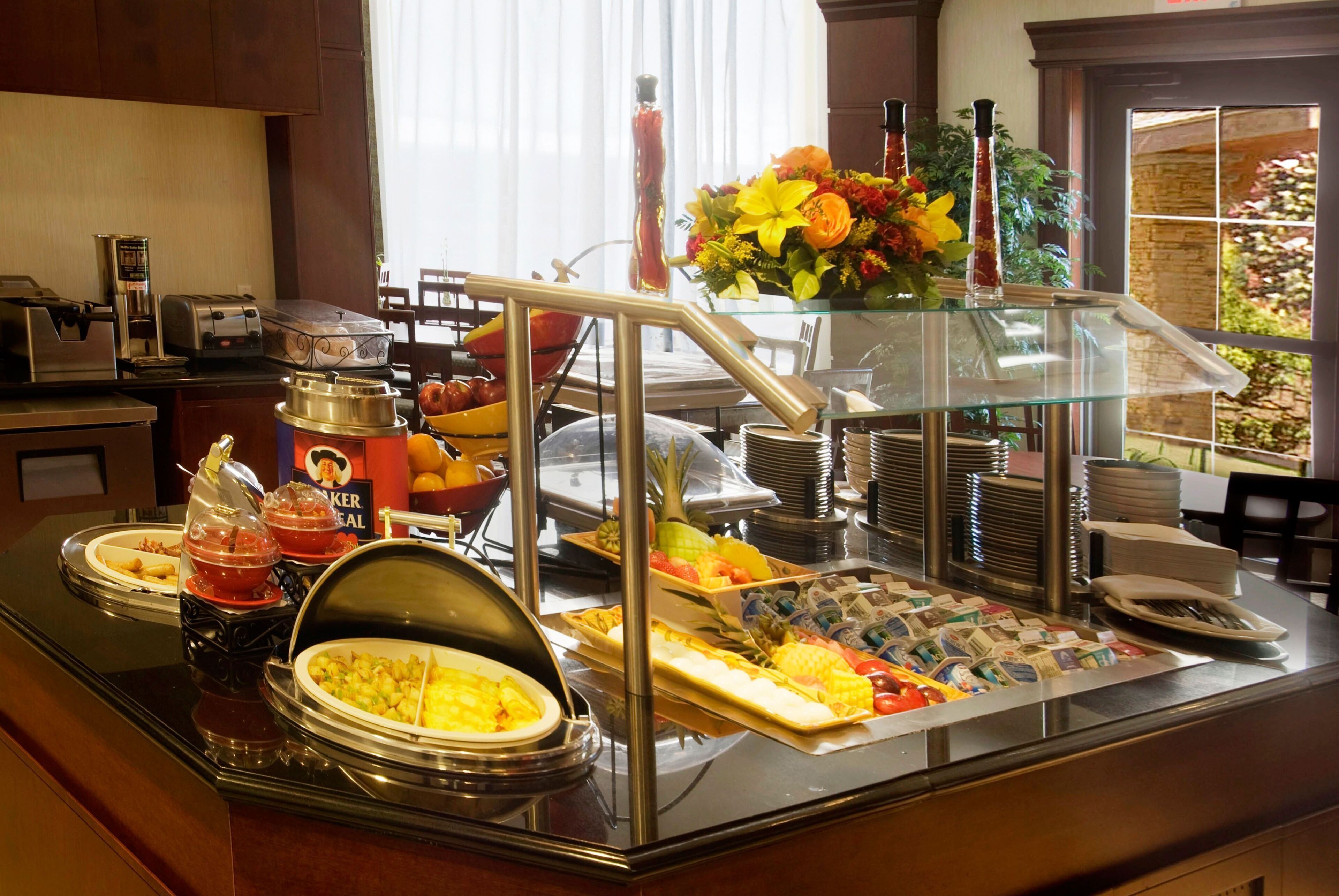 A buffet setup with various food items, a coffee machine, and a flower arrangement.