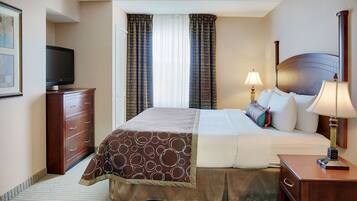 A hotel room with a bed, a television, a desk with a lamp, and a window with curtains.