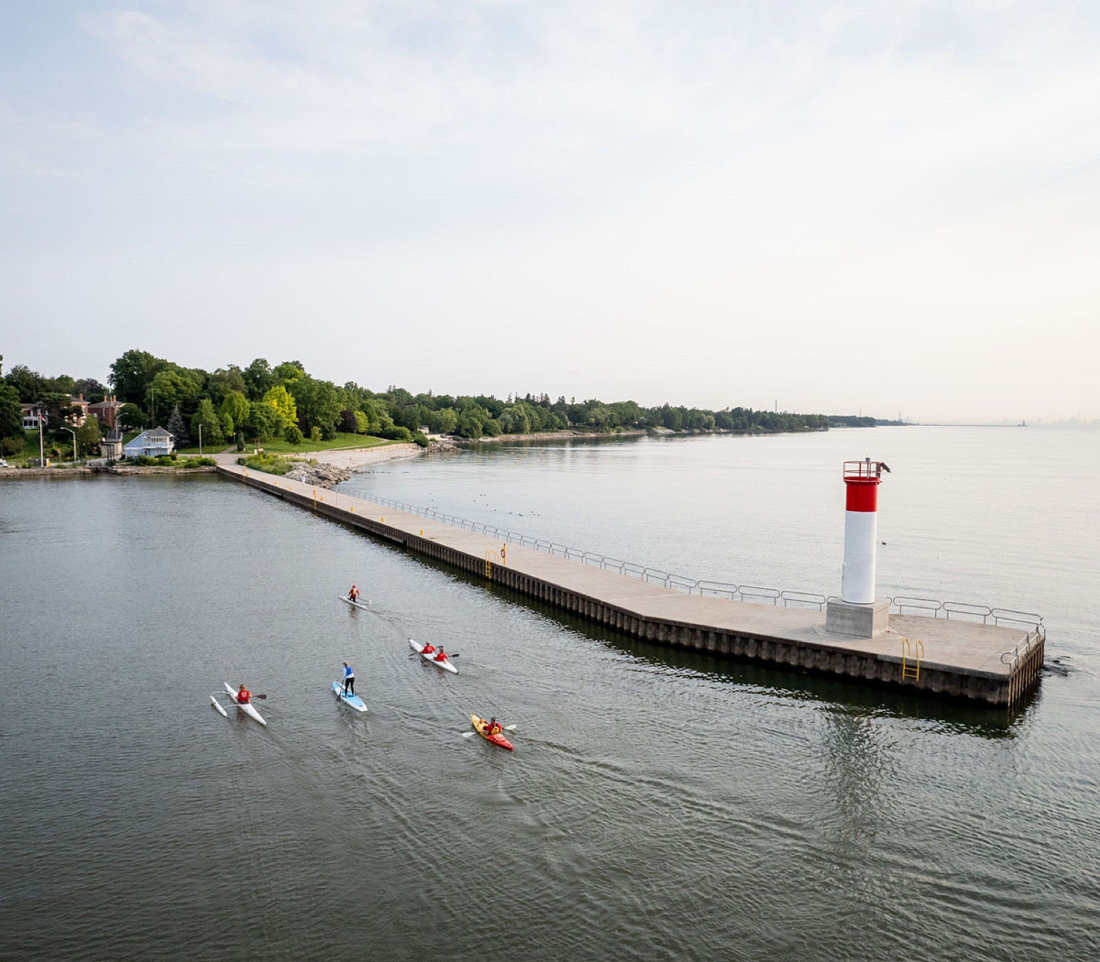 A calm waterfront with a pier extending into the water, a lighthouse, and several kayaks.