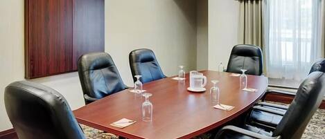 A conference room with a wooden table, black leather chairs, and a whiteboard.