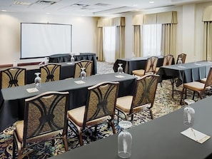 A conference room with tables, chairs, a projector screen, and a carpeted floor.