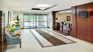 A hotel lobby with a reception desk, a waiting area with chairs, a reception counter, and a large glass door leading outside.