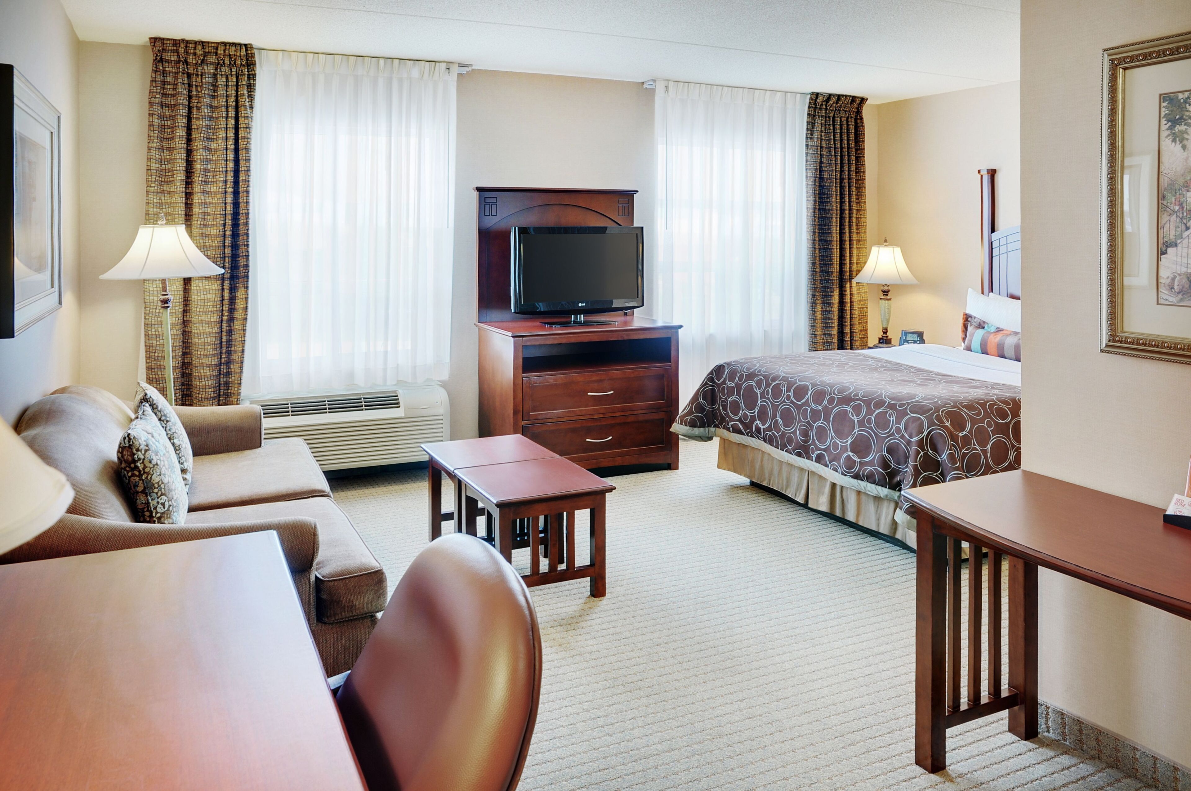 Una habitación de hotel con cama, escritorio, silla, televisor y sofá.