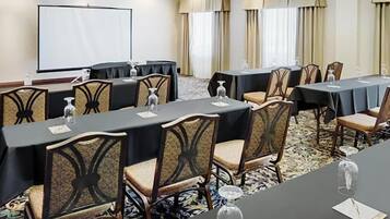 A conference room with tables, chairs, a projector screen, and a carpeted floor.