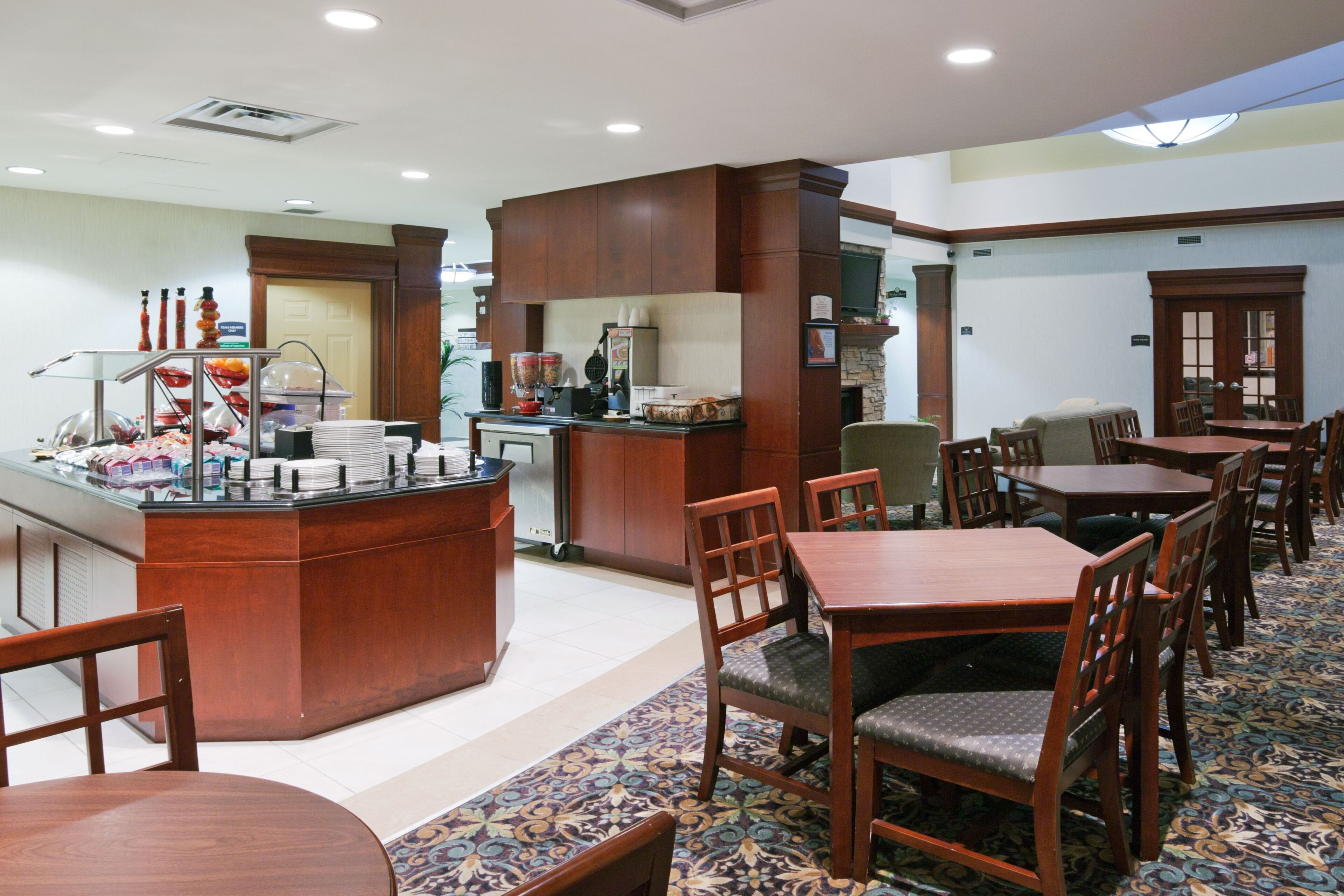 A hotel dining area with a buffet station, seating arrangements, and a television.