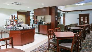A hotel dining area with a buffet station, seating arrangements, and a television.