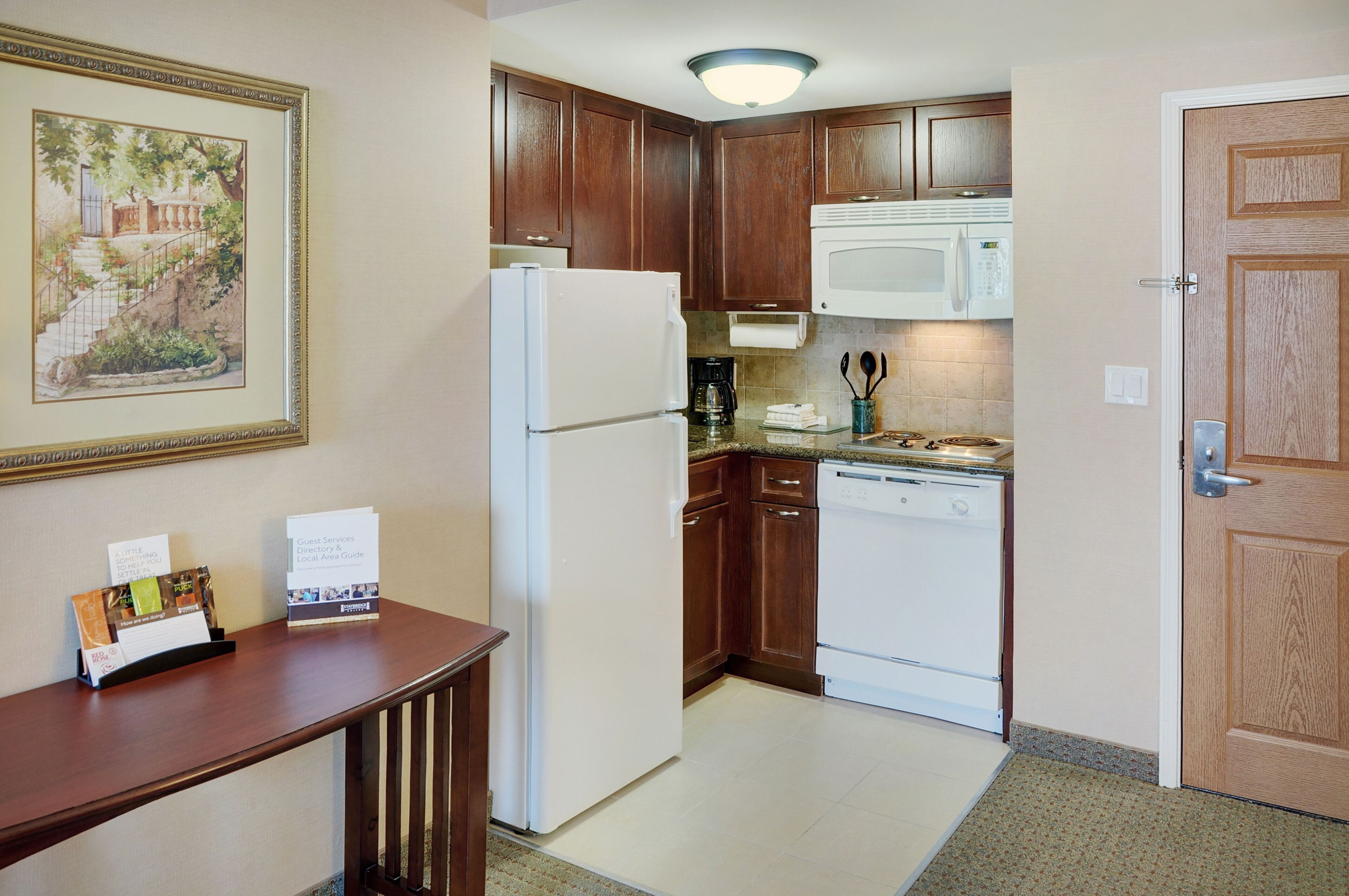 A compact kitchen with wooden cabinets, a white refrigerator, a microwave, and a dishwasher.