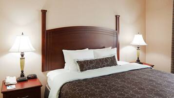 A hotel room with a large bed, two bedside tables with lamps, a nightstand with a phone and a notepad, and a wall clock.