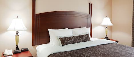 A hotel room with a large bed, two bedside tables with lamps, a nightstand with a phone and a notepad, and a wall clock.