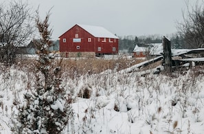 Une grange rouge avec une enseigne indiquant « Baker Creek, ferme pédagogique pour enfants », dans un champ enneigé.