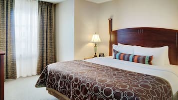 Une chambre d’hôtel avec un grand lit, une table de chevet, une lampe et une fenêtre avec des rideaux.