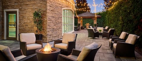 An outdoor patio area with wicker furniture, a fire pit, and string lights.