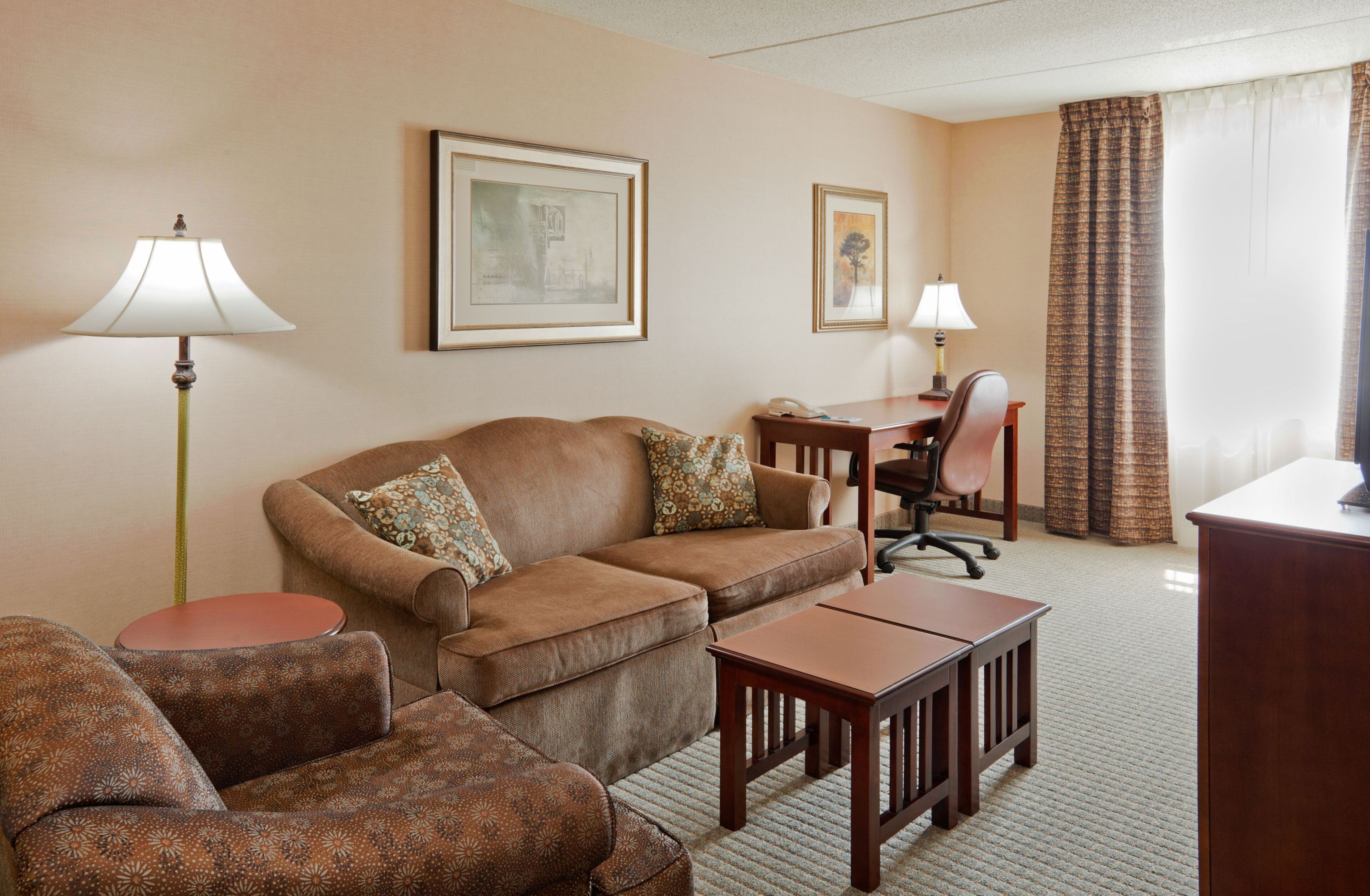 A hotel room with a sofa, armchair, desk, and lamp.