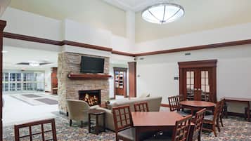 Un hall de hotel con chimenea de piedra, un televisor de pantalla plana en la pared, un área de descanso con sofás y sillones, y un piso con diseño.