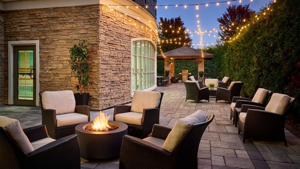 An outdoor patio area with wicker furniture, a fire pit, and string lights.