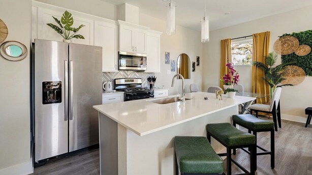 A modern kitchen with a central island, stainless steel appliances, and a dining area with bar stools. - 3BR Gated Community Houston Home  + Parking (Houston)