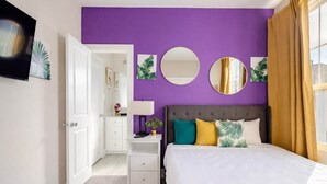 A bedroom with a purple wall, a bed with multiple pillows, a nightstand, and a mirror. - 3BR Gated Community Houston Home  + Parking (Houston)